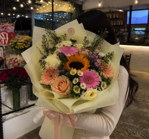 A hand-tied bouquet of sunflowers, gerberas, and roses held in the shop