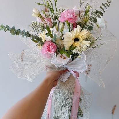 A hand-tied bouquet of cream gerberas, pink carnations and eucalyptus, held up in the KinLove Flowers + Coffee Uptown flower studio